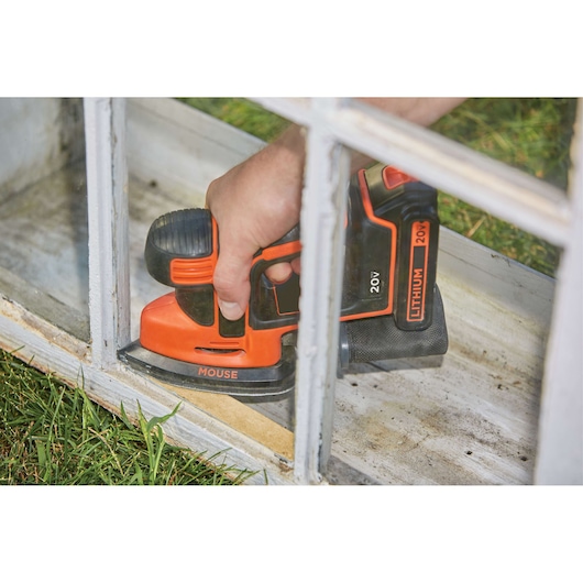 Photo de la ponceuse sans fil BLACKDECKER BD2KITCDDS ponçant un cadre de fenêtre, couleur orange et noire.