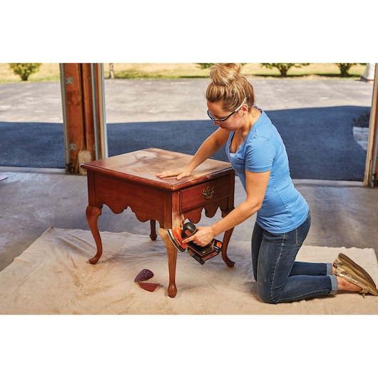 Photo du BLACKDECKER BD4KITCDCMSL ponceuse sans fil ponçant une table en bois dans un garage.