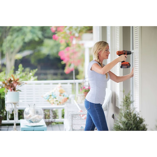Photo d'une personne utilisant une perceuse sans fil BLACK+DECKER du kit de photographie BD4KITCDCMSL pour installer des volets sur une véranda.