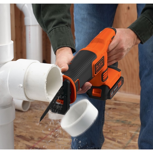 Photographie de la scie réciproque BLACK+DECKER BDCR20C découpant un tuyau en PVC blanc en intérieur.