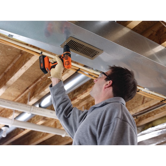 Personne utilisant la perceuse sans fil BLACKDECKER LDX120C pour installer une grille de ventilation au plafond brut.