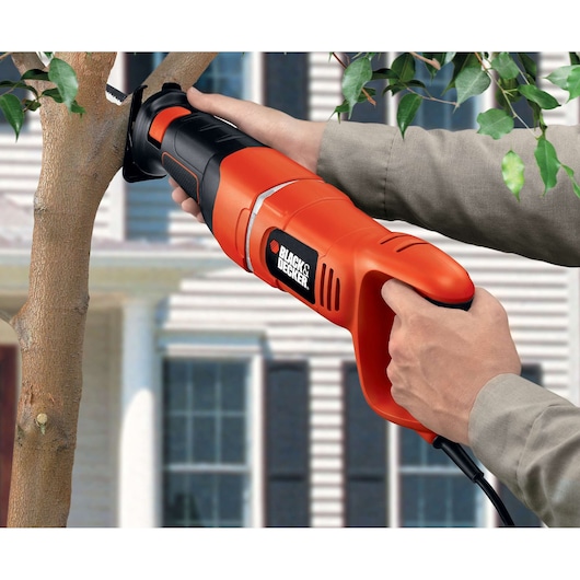 Scie alternative BLACK+DECKER RS500 coupant une branche d'arbre en extérieur, vue rapprochée de l'outil en utilisation.