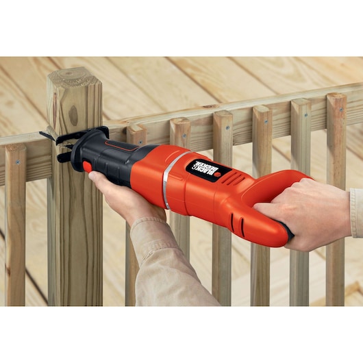 Photographie de la scie sabre BLACK+DECKER RS500 coupant un poteau en bois, design orange et noir visible.