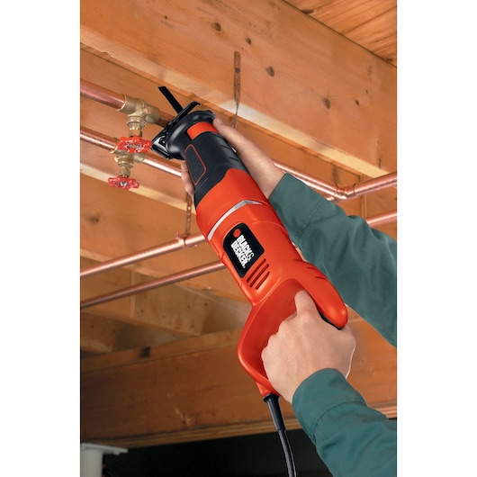 Photographie de la scie alternative BLACKDECKER RS500 découpant un tuyau en cuivre près d’un plafond, utilisée par une personne.